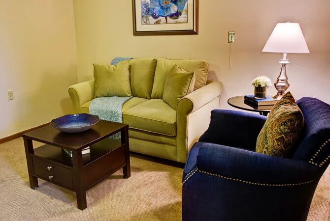 Cozy living room with a green sofa, blue armchair, and soft lighting.