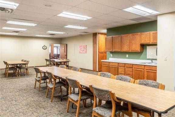 A spacious conference room with a long wooden table surrounded by chairs, featuring wooden cabinets and ceiling lights.