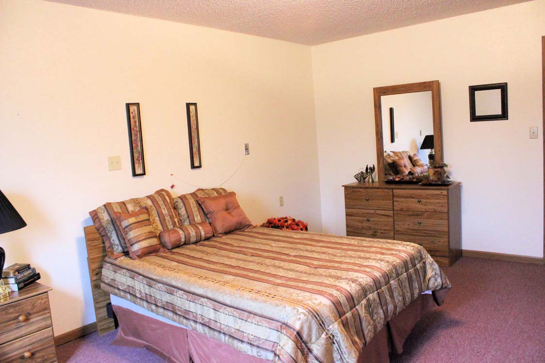 A cozy bedroom with a neatly made bed and a dresser topped with a mirror.