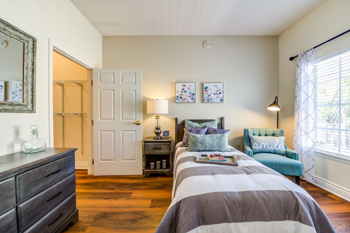 A cozy bedroom featuring a neatly made bed, nightstand with a lamp, and wooden flooring.