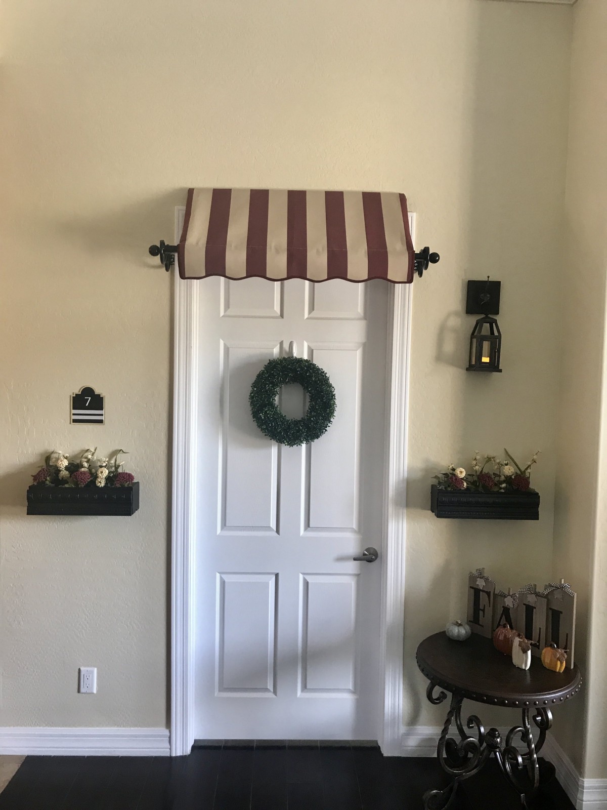 A stylish door with a striped awning and a wreath, surrounded by decorative shelves.