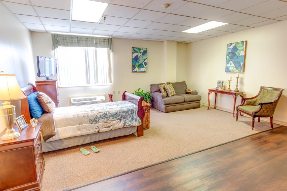 A spacious bedroom with a bed, couch, and table, featuring warm lighting and decor elements.
