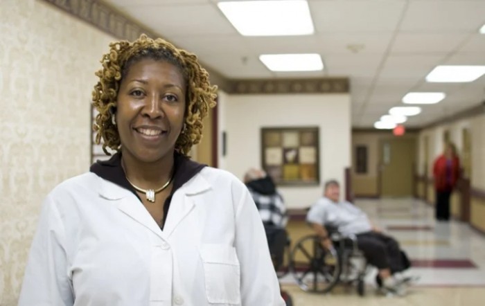A healthcare professional smiling in a hospital hallway with patients in the background.
