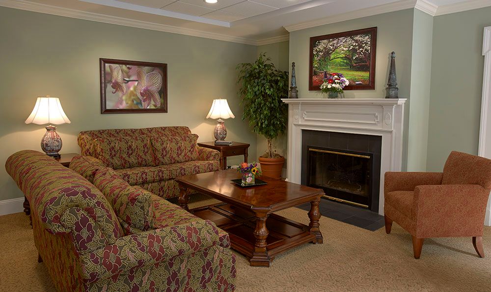 A cozy living room with a sofa, coffee table, and fireplace, decorated with paintings and plants.