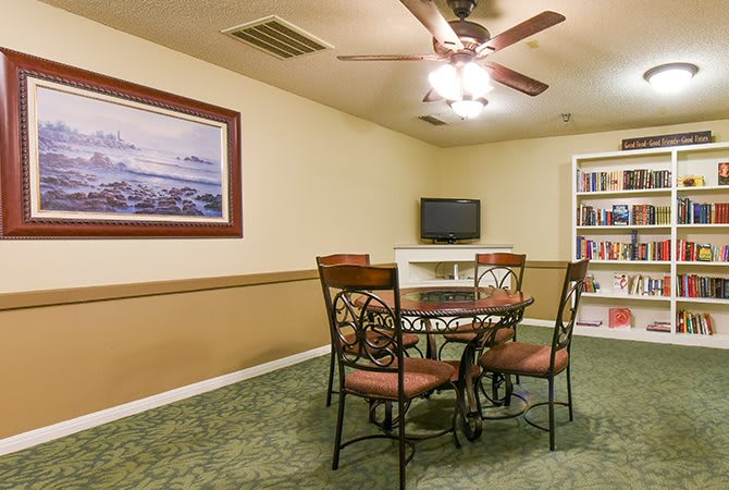 A cozy living room with a small round table and chairs, a TV on a stand, and bookshelves in the corner.