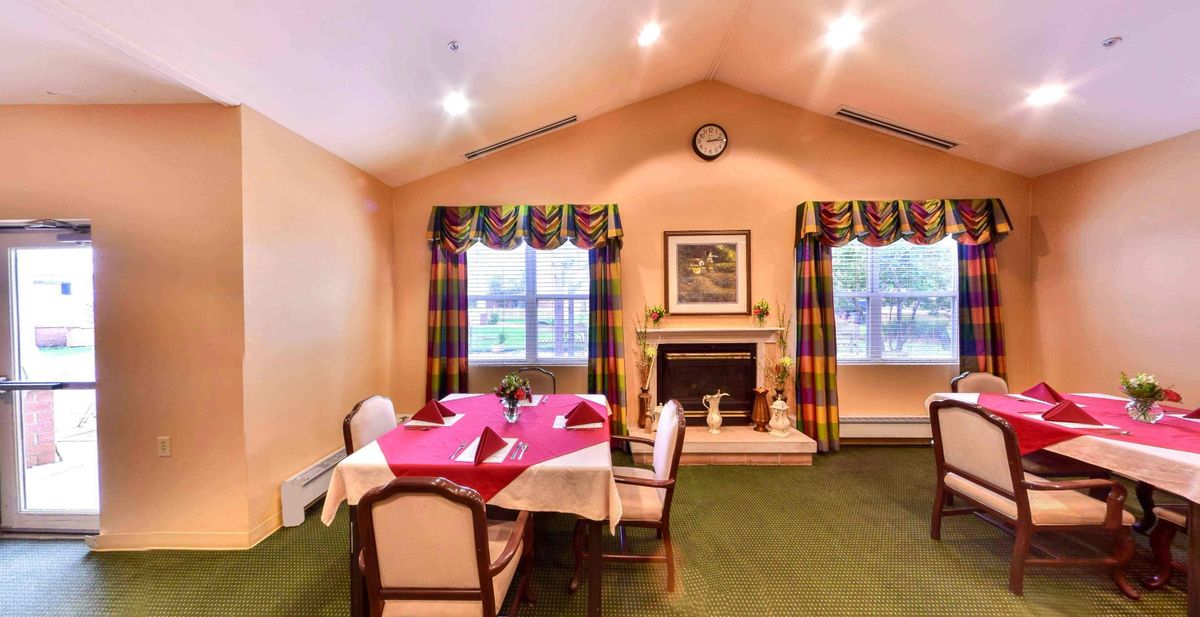 A cozy dining room with a table set for guests, featuring a fireplace and large windows with colorful curtains.