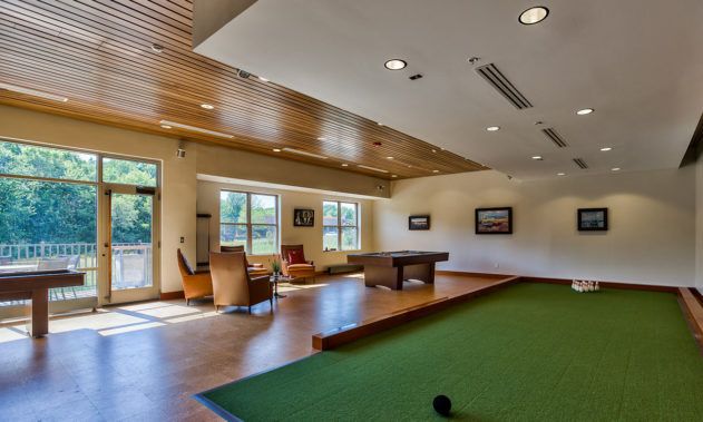 A spacious lounge featuring a pool table, green carpet, and comfortable seating near large windows.