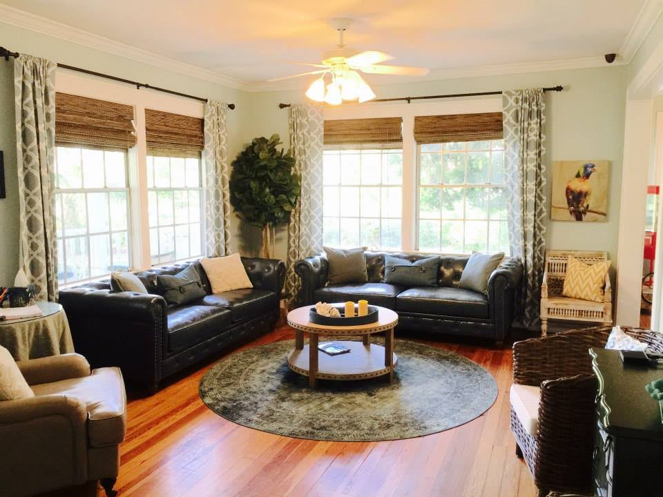 A cozy living room with ample natural light, featuring leather sofas and a central coffee table.
