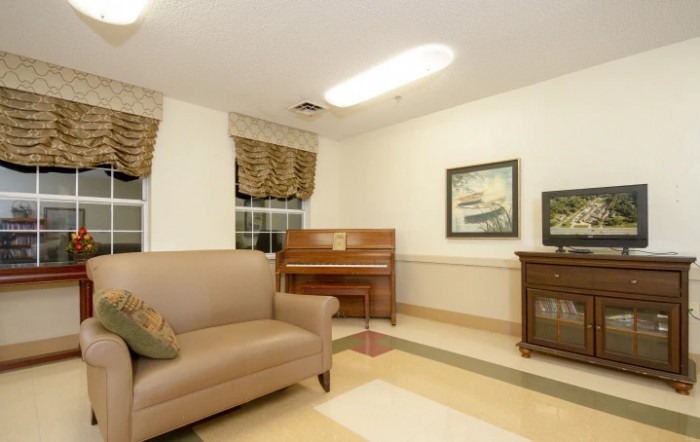 A cozy living room featuring a sofa, upright piano, and framed artwork on the walls.