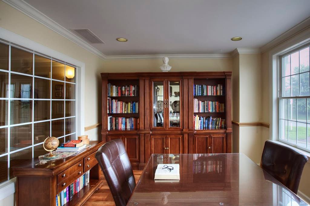 A well-organized office with a wooden bookshelf filled with books and a desk with a chair.