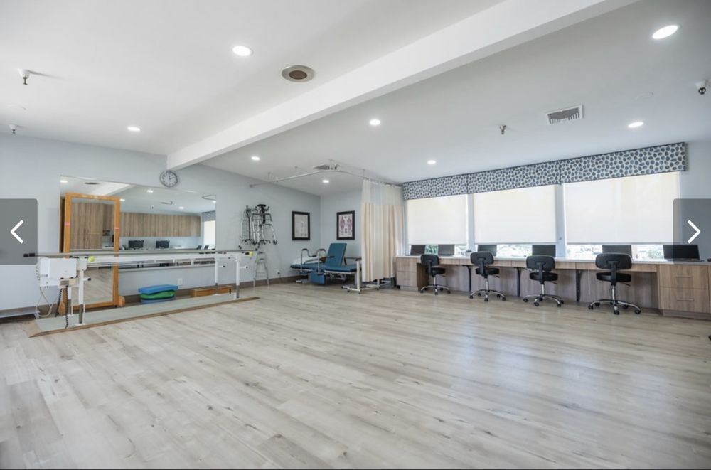 A spacious office area with desks and chairs, well-lit by natural light from large windows.