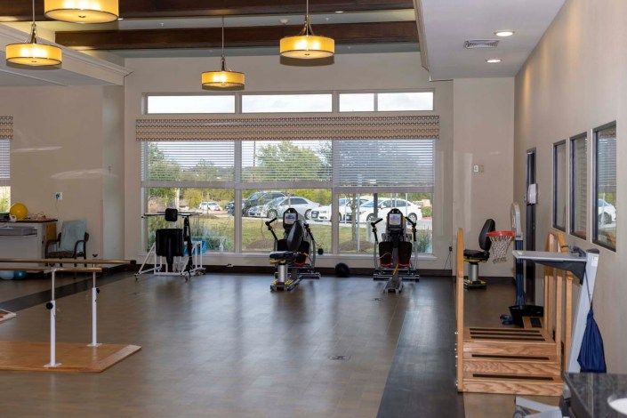 A spacious gym with exercise equipment, including treadmills and stationary bikes, near large windows.