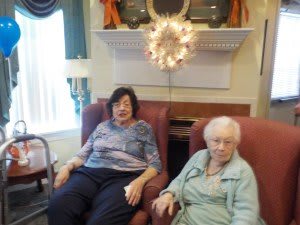 Two elderly women seated in a living room setting.