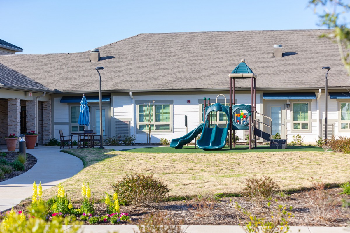 A backyard playground with a slide and a residential building in the background.
