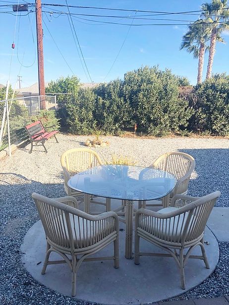 A cozy outdoor patio area with a glass table and chairs surrounded by greenery.