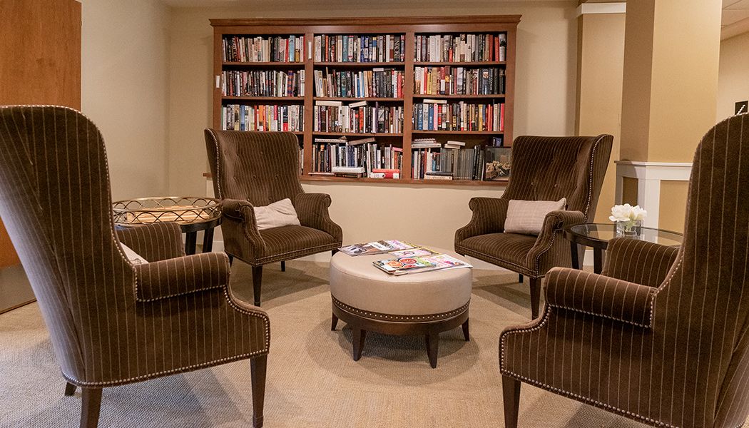 A cozy reading room featuring bookshelves and comfortable armchairs around a coffee table.