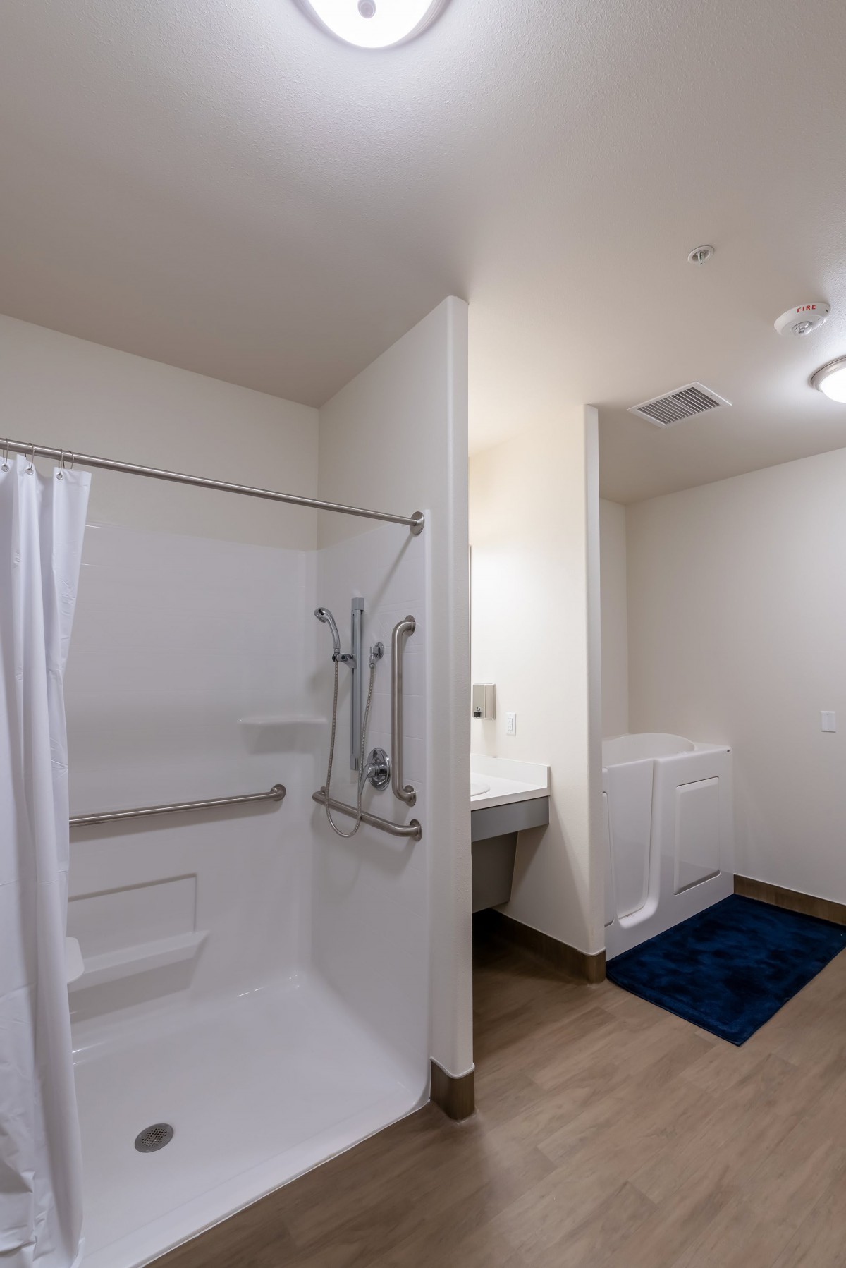 An accessible bathroom with a shower featuring grab bars and a curtain, alongside a sink and a tiled floor.