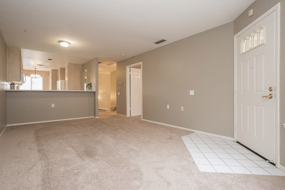 Spacious living area with neutral tones and carpet flooring, featuring an open design leading to the kitchen.