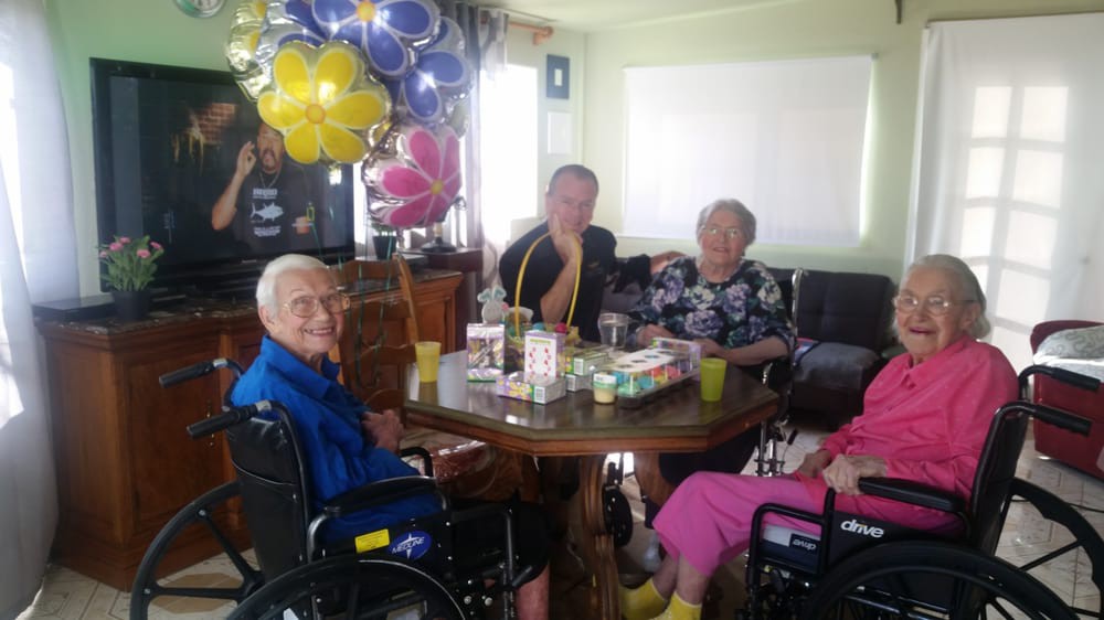 A group of elderly people sitting around a table, celebrating with balloons.