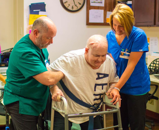 Healthcare workers assist an elderly man using a walker during rehabilitation.