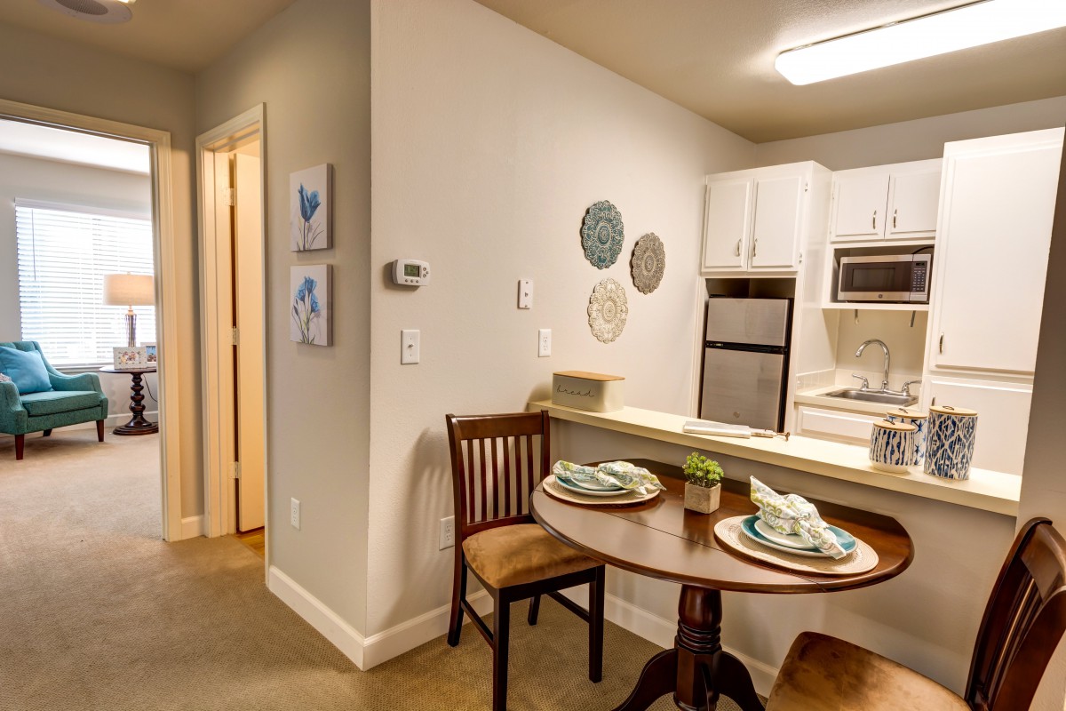 A cozy kitchen and dining area with a small round table set for two, featuring modern appliances and wall decor.