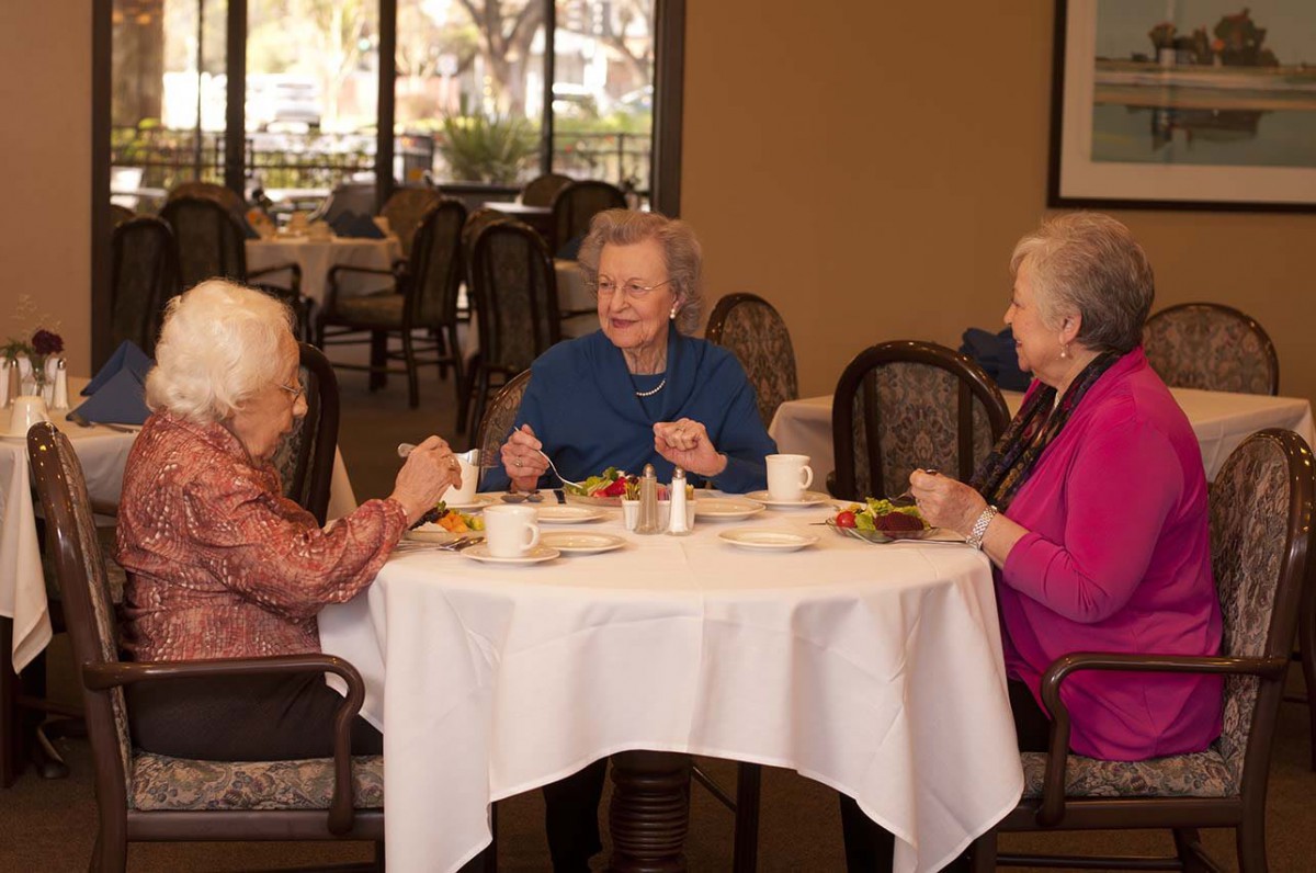 Three elderly women enjoying a meal and conversation at a restaurant.