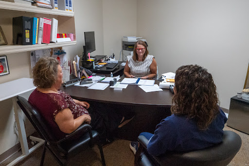 A group discussion in an office setting, with individuals seated around a desk.