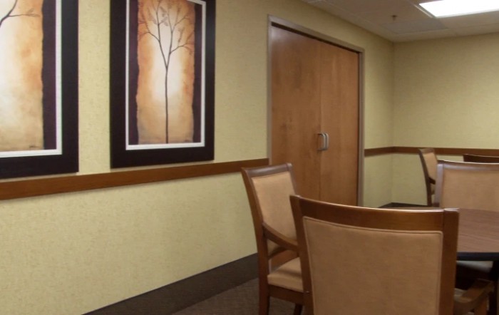 A waiting room with chairs, a painting on the wall, and a closed wooden door.