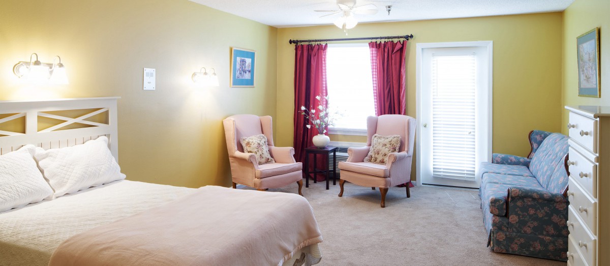 A cozy bedroom with two armchairs, a window with red curtains, and soft lighting.