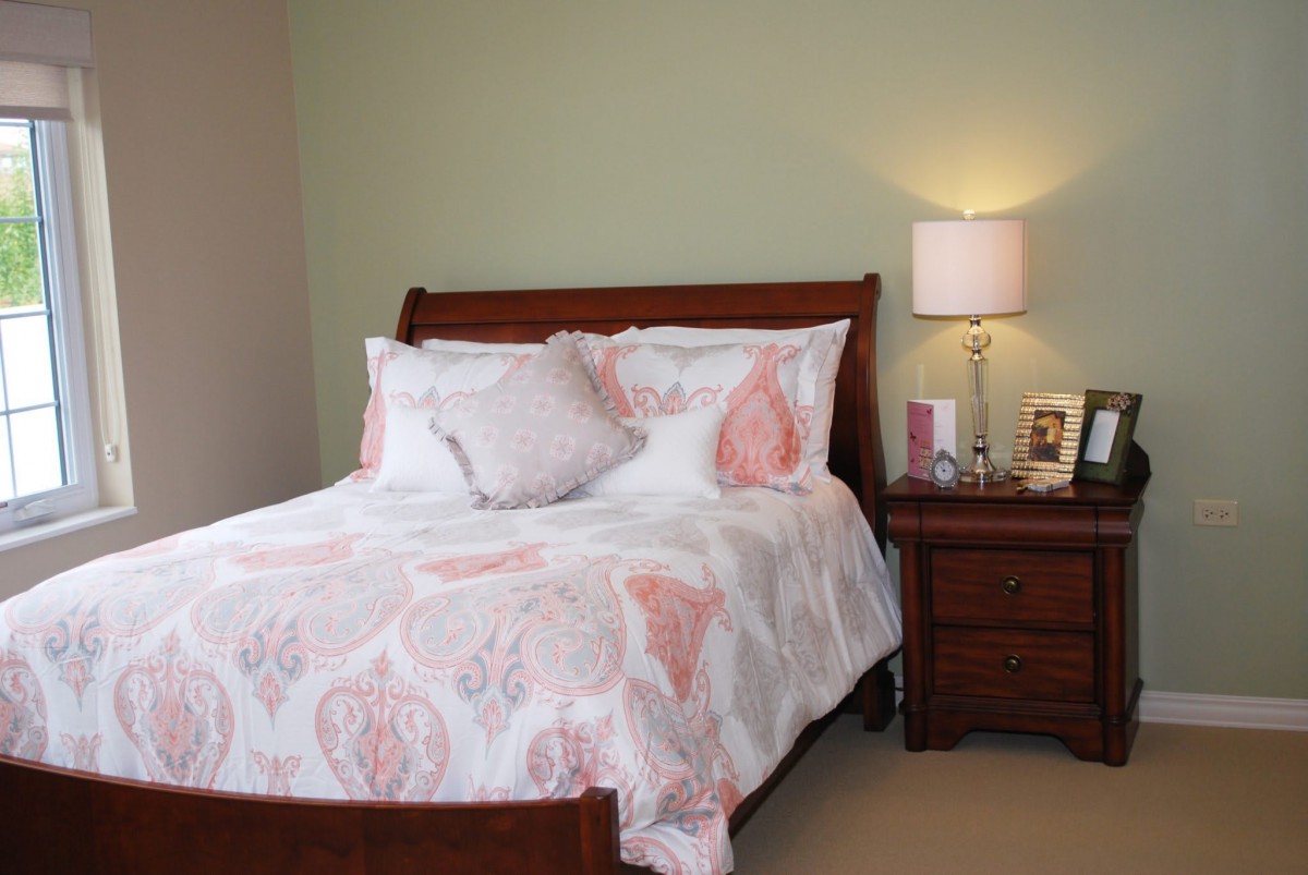 A cozy bedroom with a neatly made bed and a nightstand with a lamp.