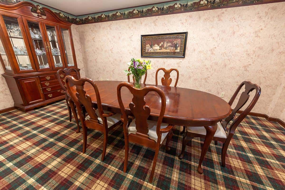 A traditional dining room with an elegant wooden table, matching chairs, patterned carpet, and floral decor.