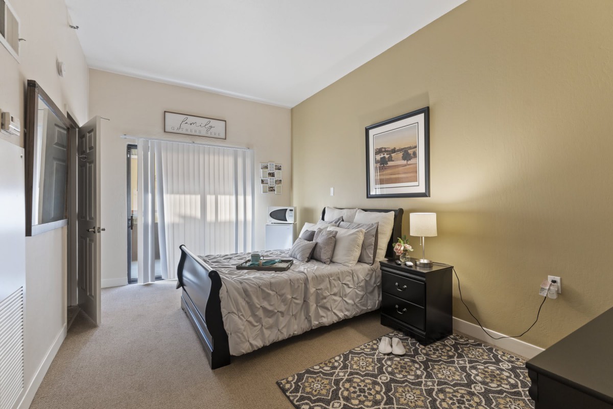 A cozy bedroom with a neatly made bed, nightstand, and lamp alongside decorative wall art.