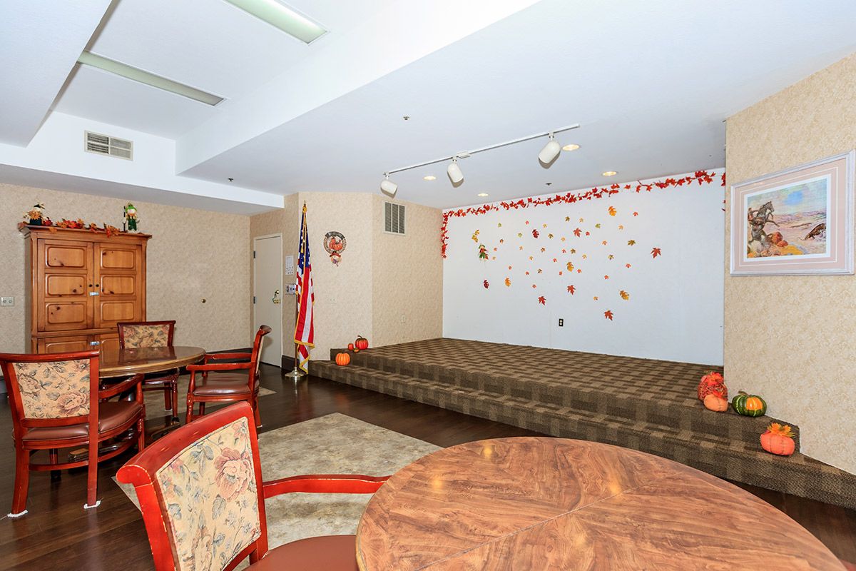 A community room featuring a small stage, seating area, and decorative wall.