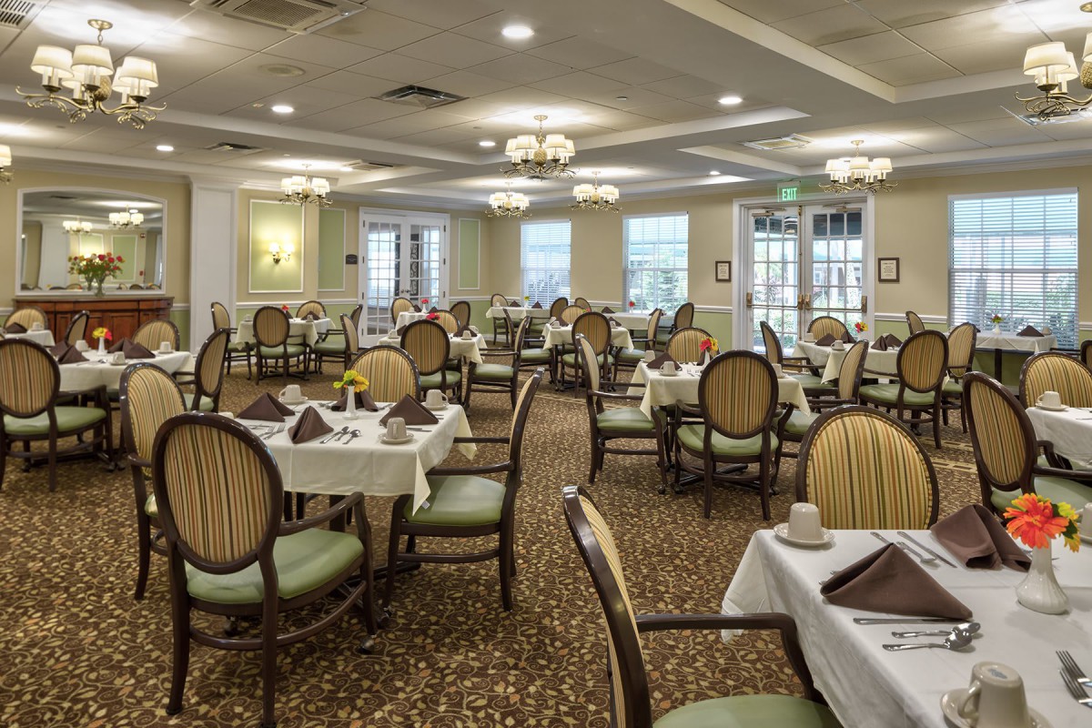 An elegant dining room with neatly arranged tables and chairs, featuring chandeliers and a carpeted floor.