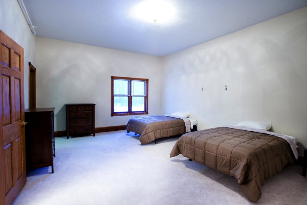 A spacious bedroom with two single beds, a dresser, and a large window providing natural light.