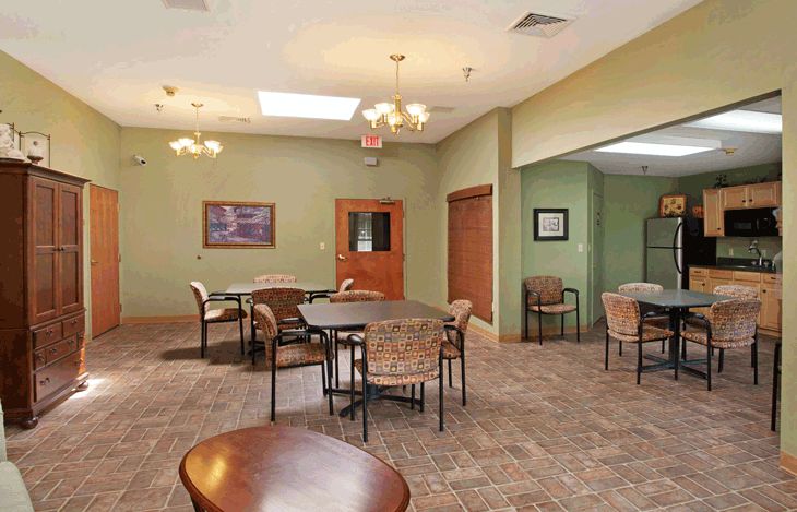 A spacious dining area with multiple tables and chairs set against green walls, featuring elegant lighting fixtures.
