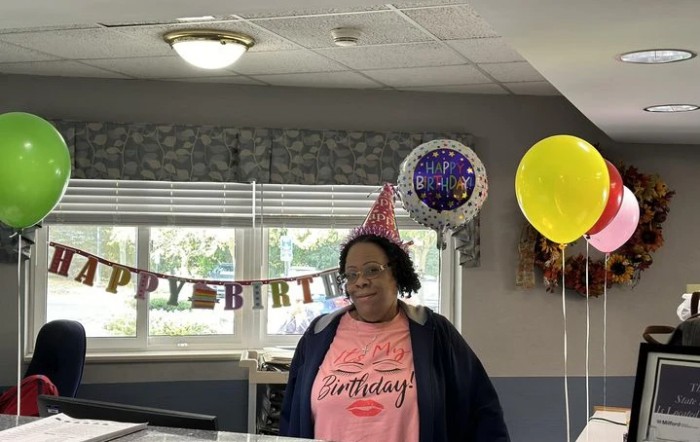 A person wearing a party hat at a birthday celebration with balloons and decorations.
