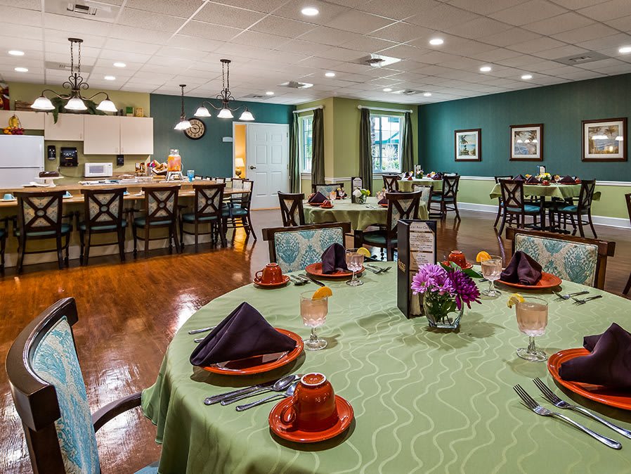 An elegantly set dining room with green tablecloths, vibrant flowers, and neatly arranged chairs, creating a welcoming atmosphere.