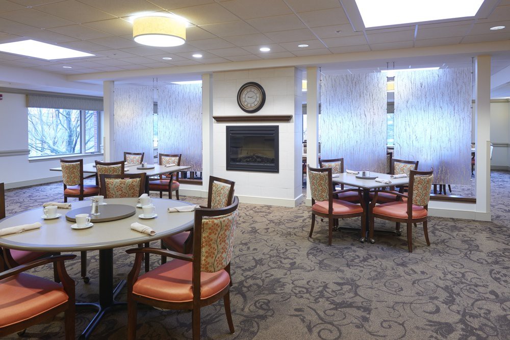 A cozy dining room with multiple tables and chairs, featuring a central fireplace.