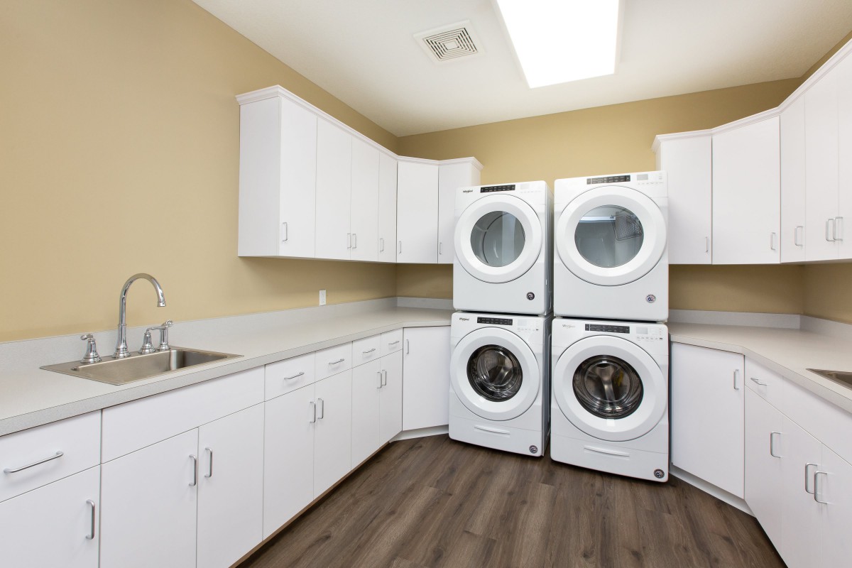A modern laundry room featuring four stacked washers and dryers, with ample white cabinetry and counter space.