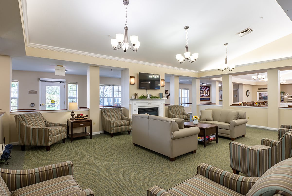A cozy and well-lit living room with multiple seating arrangements centered around a fireplace, featuring sofas, armchairs, a coffee table, and overhead chandeliers.