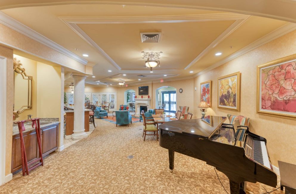 A spacious and well-lit lounge featuring a piano, artwork on the walls, and comfortable seating areas.