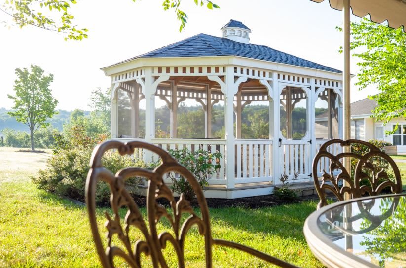 A charming white gazebo in a sunlit garden, surrounded by outdoor furniture.