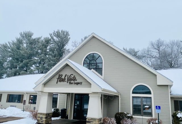 A snow-covered building with a storefront surrounded by trees in winter.