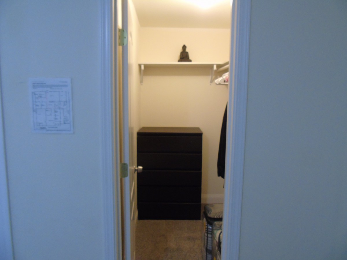 A small walk-in closet with a dresser and hanging clothes.