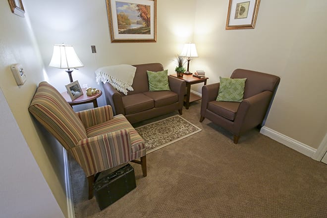A cozy living room with sofas and armchairs arranged around a rug, complemented by warm lighting and decorative artwork.