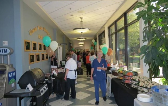 A hallway event with people, balloons, and food tables on display.