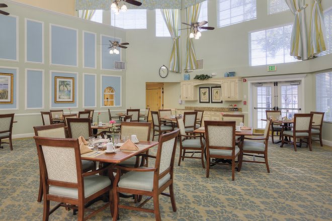A well-lit dining room with arranged tables and chairs, featuring large windows and elegant decor.