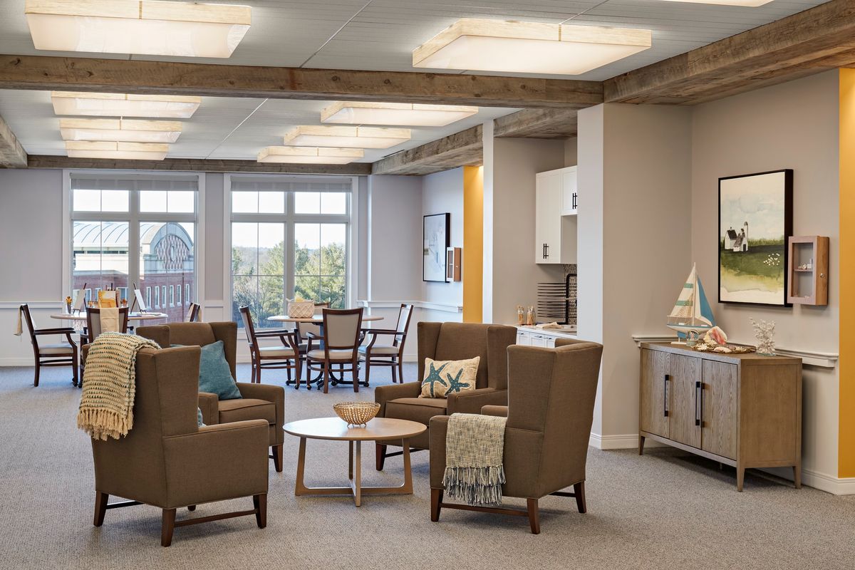 A cozy living room with armchairs and a coffee table, adjacent to a dining area with large windows.