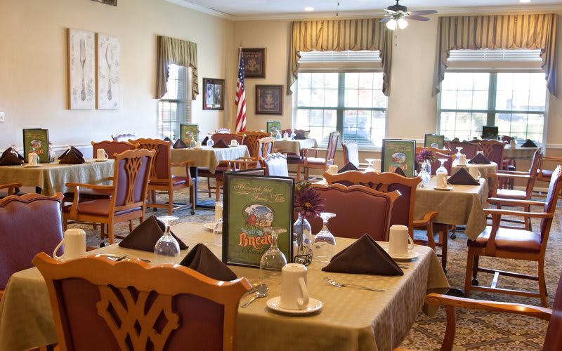 A well-arranged dining area featuring neatly set tables, chairs, and windows allowing natural light.
